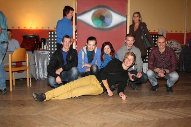 Eine Gruppe junger Leute posiert vor einem bemalten Hintergrund mit einem Auge.
