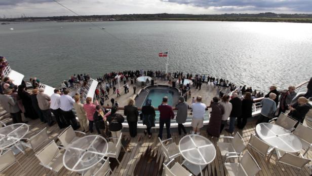 Viele Menschen versammeln sich auf dem Deck eines Kreuzfahrtschiffes mit Pool und dänischer Flagge.