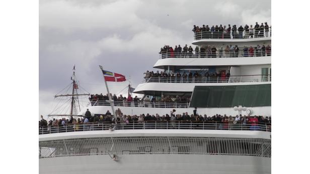 Viele Menschen stehen auf den Decks eines Kreuzfahrtschiffes unter einer bewölkten Himmel.