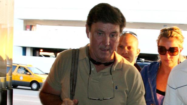 Ein Mann mit Sonnenbrille um den Hals steht vor einem gelben Taxi.