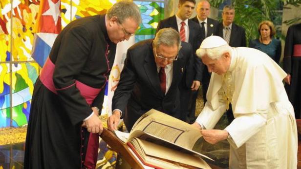 Papst Benedikt XVI. betrachtet mit anderen Würdenträgern ein aufgeschlagenes Buch.