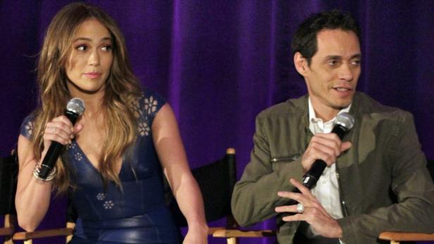 Jennifer Lopez und Marc Anthony halten Mikrofone vor einem lila Hintergrund.