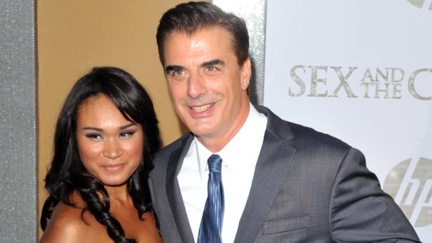 Chris Noth und Tara Wilson posieren vor einem „Sex and the City“-Logo.