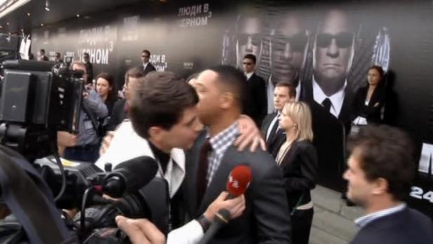 Will Smith wird auf dem roten Teppich von Reportern interviewt, im Hintergrund ein „Men in Black 3“-Poster.
