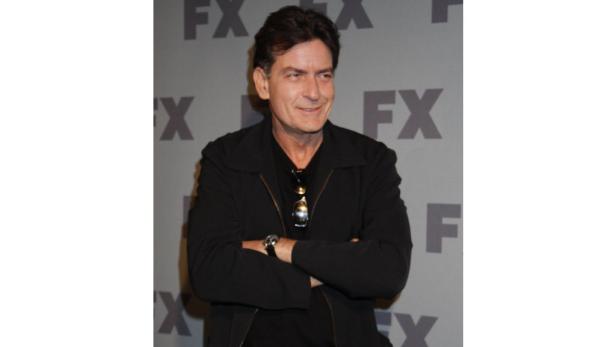 Charlie Sheen posiert mit verschränkten Armen vor einem FX-Hintergrund.