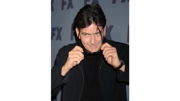 Charlie Sheen hält eine Sonnenbrille in der Hand.