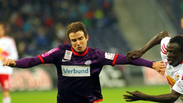 Ein Fußballspieler im lila Trikot wird von einem Gegenspieler bedrängt.