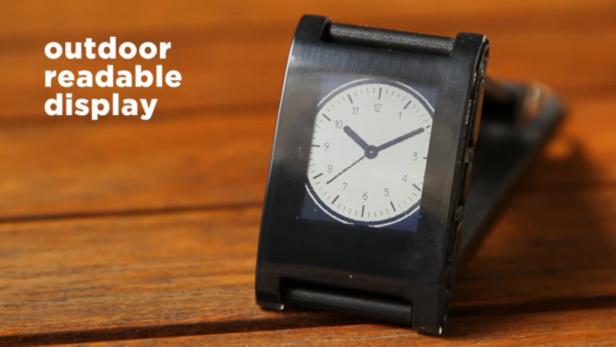 Eine schwarze Smartwatch mit einem analogen Zifferblatt auf einem Holztisch.