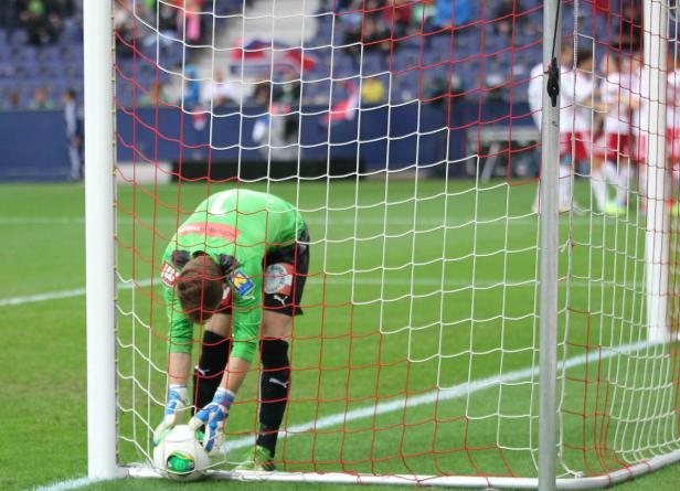 Ein Torwart in grüner Kleidung hebt einen Fußball im Tornetz auf.
