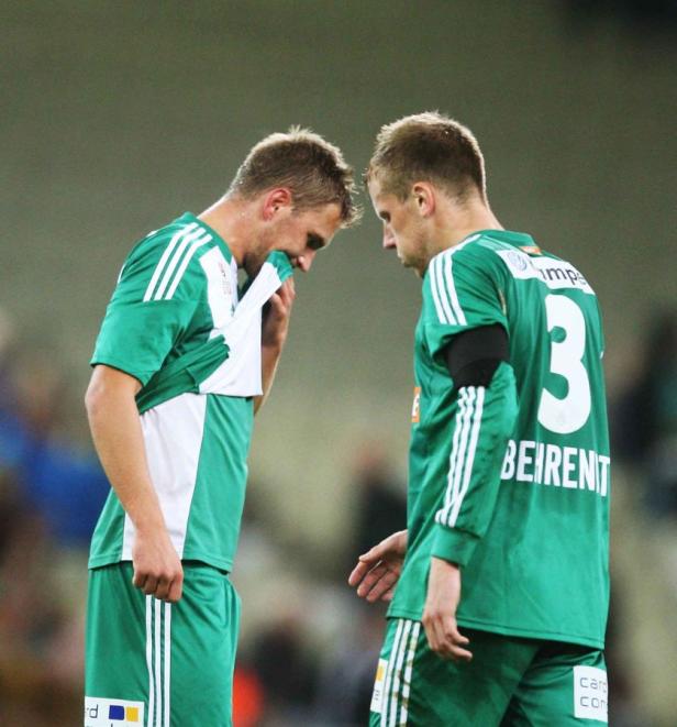 Zwei Fußballspieler in grünen Trikots stehen nachdenklich nebeneinander.