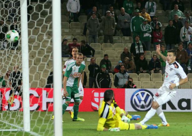 Ein Fußballspieler schießt den Ball ins Tor, während der Torwart am Boden liegt.