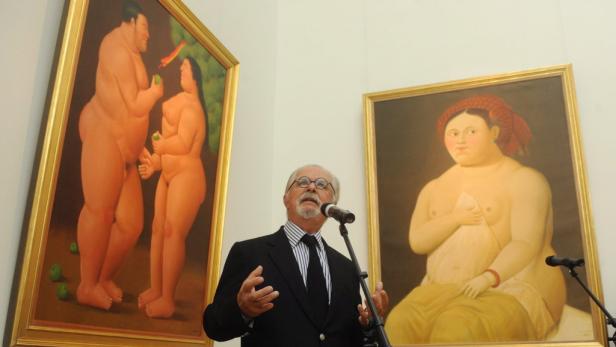 Ein Mann spricht vor zwei Gemälden von üppigen Figuren, möglicherweise von Fernando Botero.