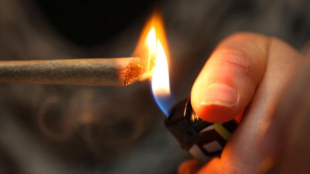 Eine Hand zündet mit einem Feuerzeug eine Zigarette an.