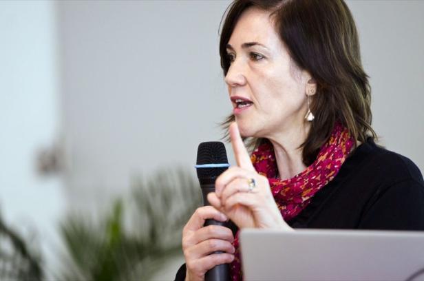 Eine Frau spricht in ein Mikrofon und gestikuliert mit dem Finger.
