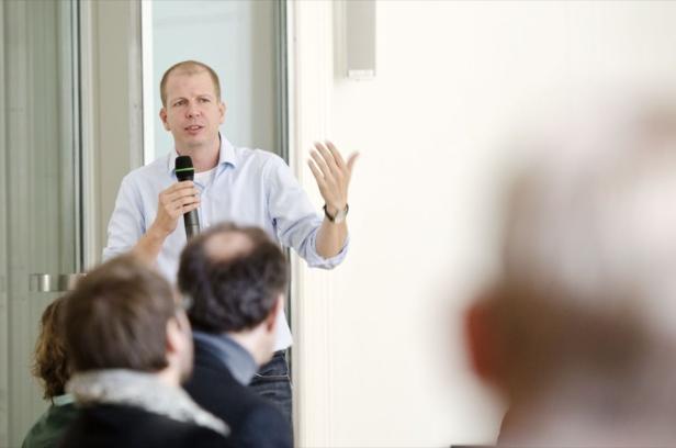 Ein Mann hält ein Mikrofon und spricht vor einem Publikum.