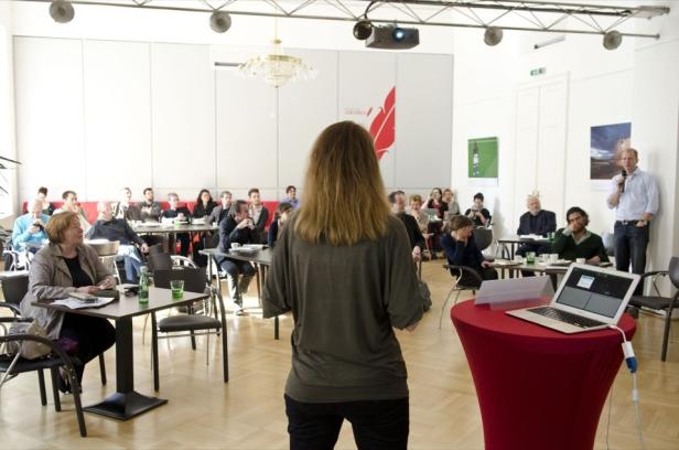 Eine Frau hält vor einem Publikum in einem Konferenzraum eine Präsentation.