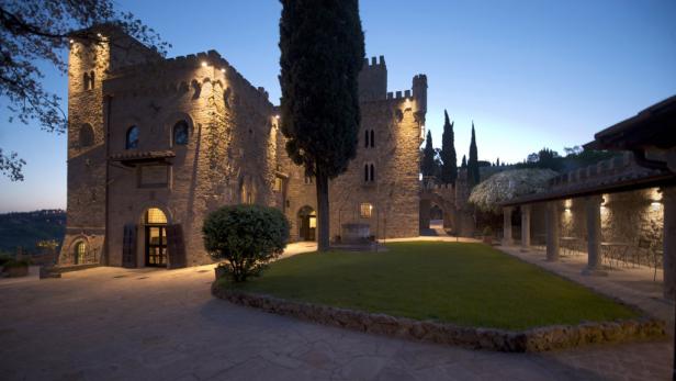 Ein beleuchtetes Schloss mit einem gepflegten Rasen im Abendlicht.