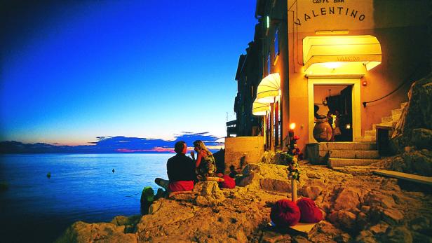 Ein Paar sitzt am Ufer vor dem Café Valentino und genießt den Sonnenuntergang.