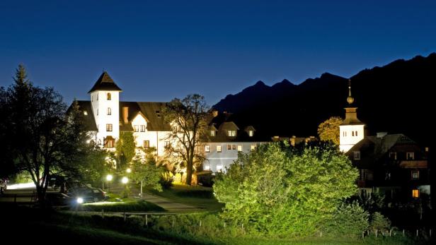 Ein beleuchtetes Schloss mit Turm vor dunklen Bergen in der Nacht.