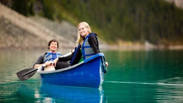 Ein Paar paddelt in einem blauen Kanu auf einem ruhigen See.
