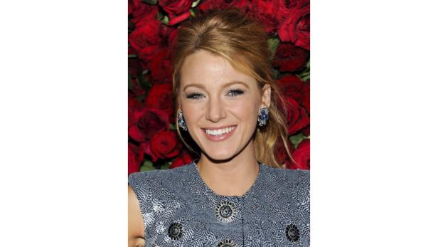 Blake Lively lächelt vor einem Hintergrund aus roten Rosen.