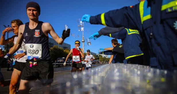 Läufer nehmen beim Berlin-Marathon Wasser von Helfern entgegen.