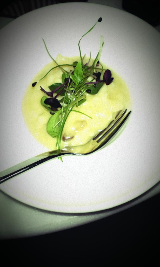 Ein Teller mit einer hellen Suppe, garniert mit frischen Kräutern und einer Gabel.