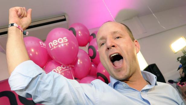 Ein Mann jubelt mit erhobener Faust vor pinkfarbenen NEOS-Luftballons.