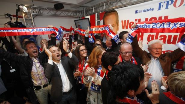 Eine Gruppe von Menschen jubelt mit roten und blauen Schärpen und Fahnen bei einer Wahlveranstaltung.