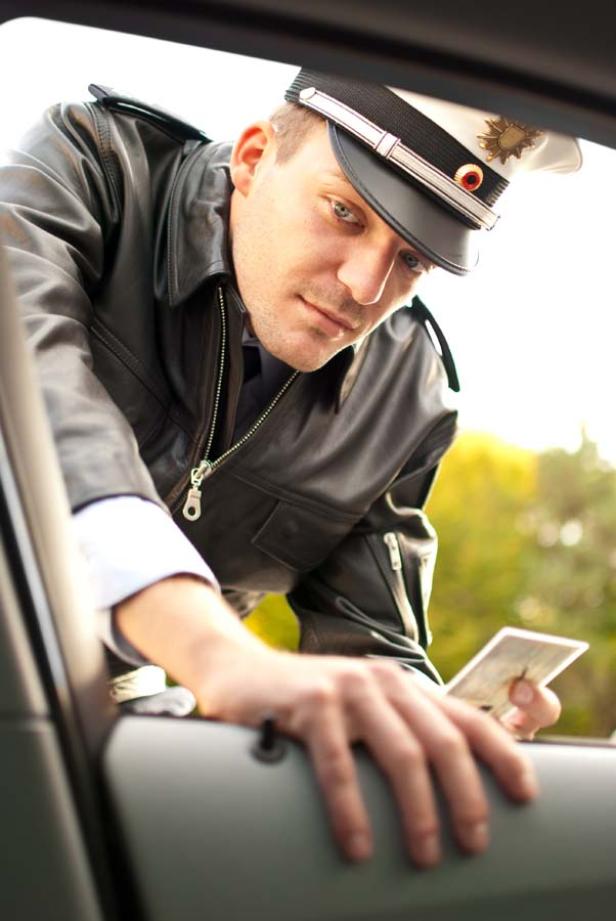 Ein Polizist in Lederjacke kontrolliert die Papiere eines Autofahrers.