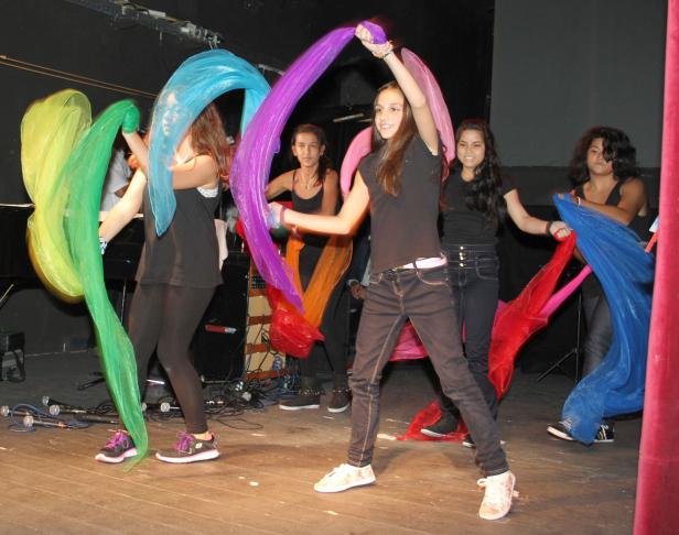 Eine Gruppe junger Frauen tanzt mit bunten Tüchern auf einer Bühne.