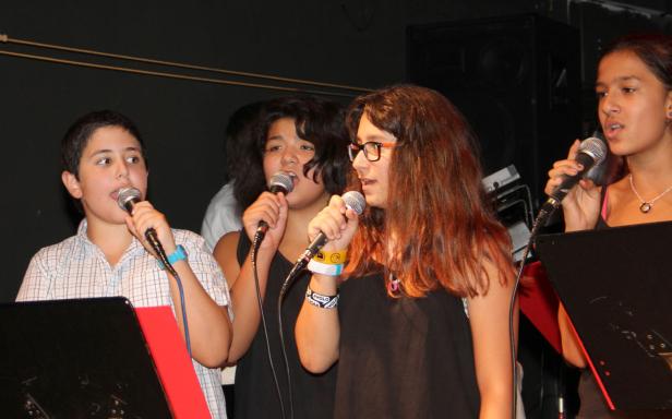 Eine Gruppe von Jugendlichen singt in Mikrofone auf einer Bühne.