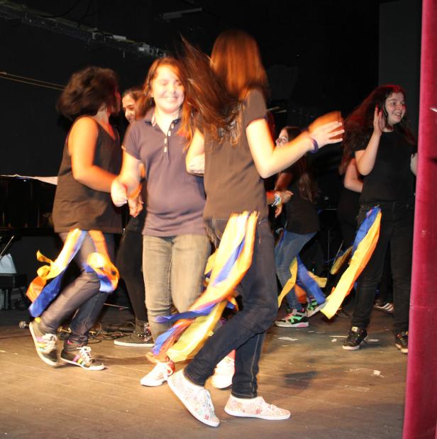 Eine Gruppe junger Frauen tanzt mit bunten Bändern auf einer Bühne.