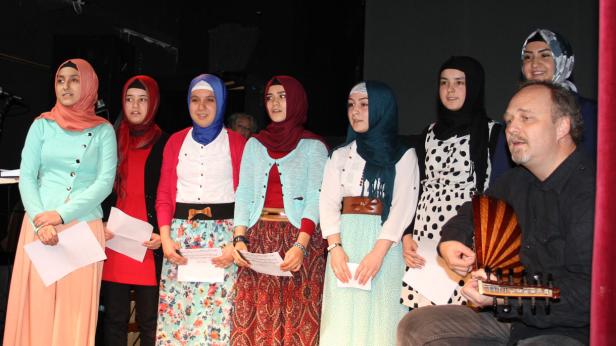 Eine Gruppe junger Frauen mit Kopftüchern steht neben einem Mann, der ein Saiteninstrument spielt.