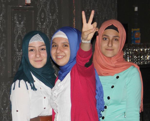 Drei junge Frauen mit Hijabs posieren lächelnd für ein Foto.