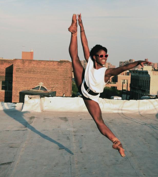 Eine Tänzerin springt mit einem Spagat auf einem Dach in der Stadt.