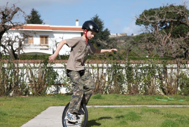 Ein Junge mit Helm fährt Einrad auf einem Gehweg im Garten.