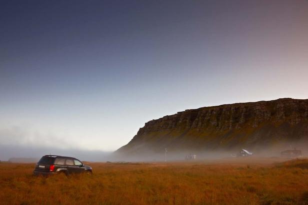 Ein dunkler SUV steht in einem Feld vor einer Klippe im Nebel.