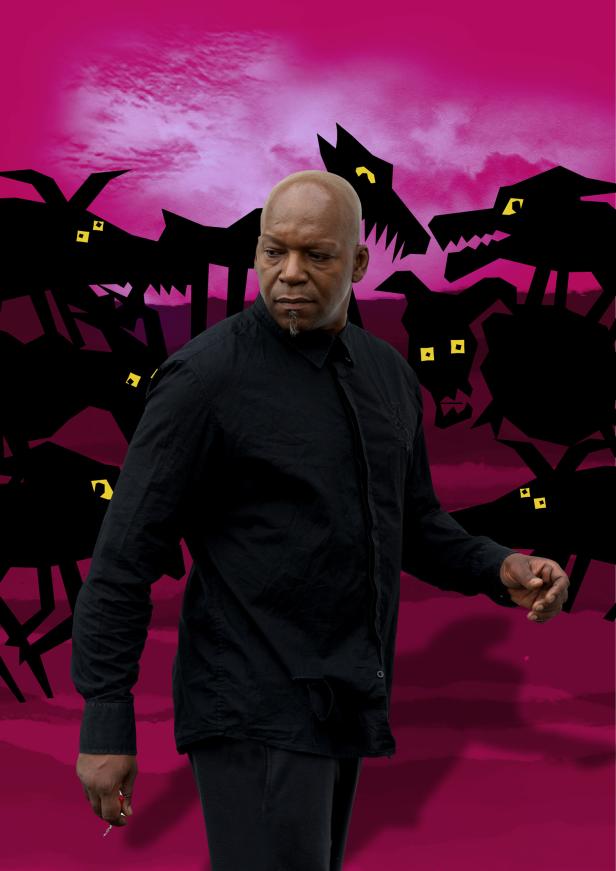 Ein Mann in Schwarz steht vor einem magenta Hintergrund mit stilisierten Wolfsköpfen.