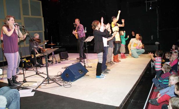 Eine Band spielt für eine Gruppe Kinder auf einer Bühne.