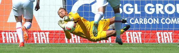 Ein Torwart in gelber Kleidung hechtet nach einem Fußball.