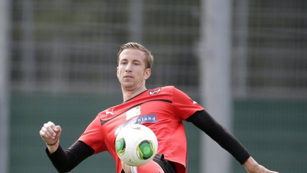 Ein Fußballspieler in rotem Trikot jongliert einen Ball mit dem Fuß.