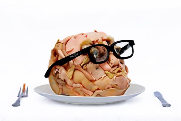 Ein Kuchen in Form eines Kopfes, bedeckt mit Babykörperteilen und einer 3D-Brille.