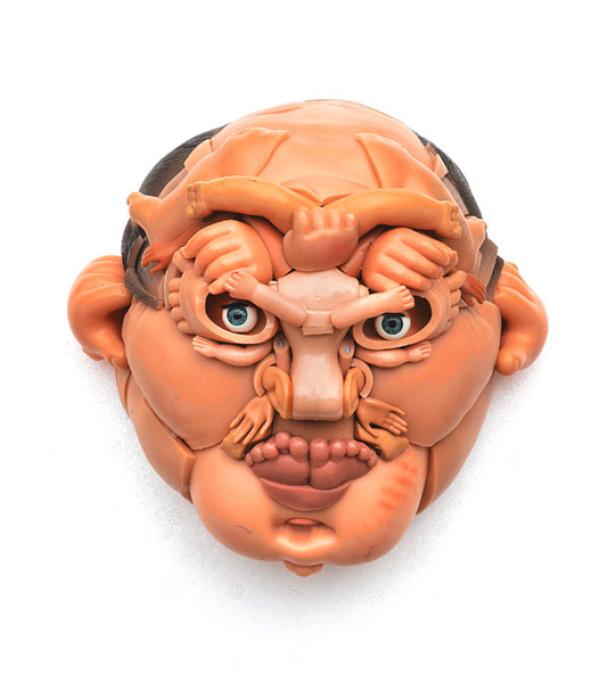 Eine skulpturale Maske, geformt aus Puppenteilen, bildet ein groteskes Gesicht.