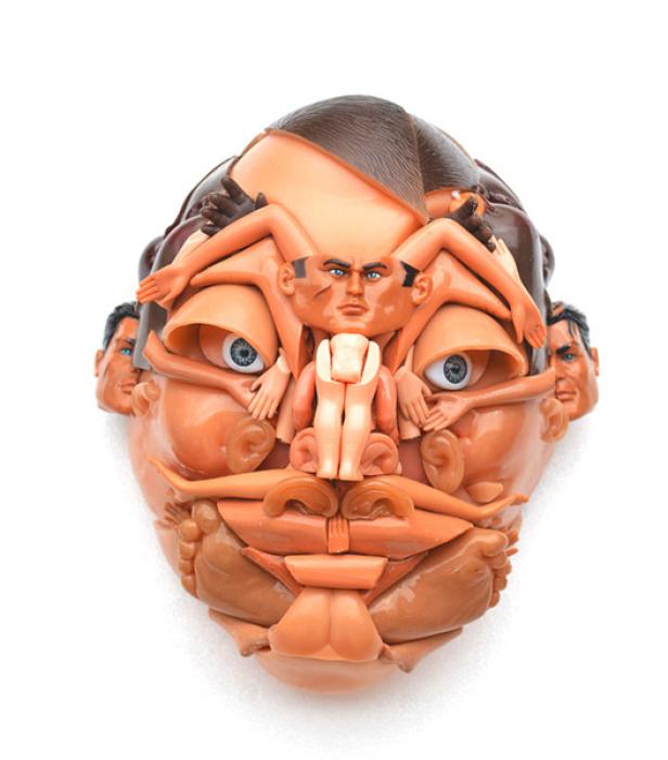 Ein Gesicht, zusammengesetzt aus verschiedenen Puppenteilen, vor einem weißen Hintergrund.
