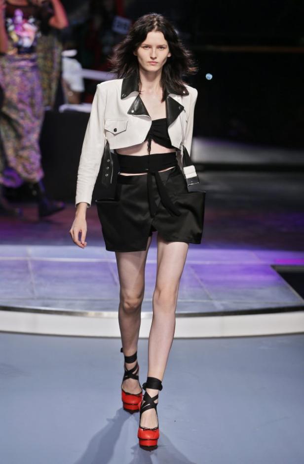 Eine Frau in einer weißen Jacke und einem schwarzen Rock auf einem Laufsteg.