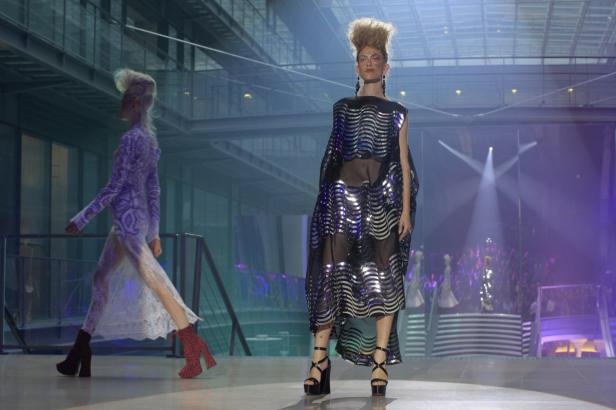 Zwei Models präsentieren extravagante Mode auf einem Laufsteg.