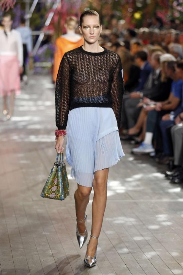 Ein Model läuft in einem schwarzen Oberteil und einem hellblauen Rock über einen Laufsteg.