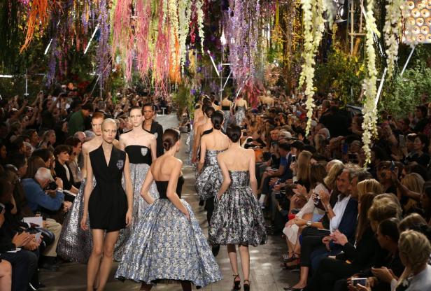 Models präsentieren Mode auf einem Laufsteg unter einem Baldachin aus Blumen.