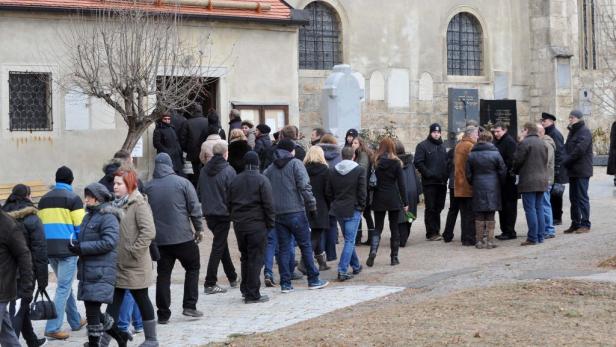 Eine Menschenmenge versammelt sich vor einem Gebäude, möglicherweise für eine Beerdigung.
